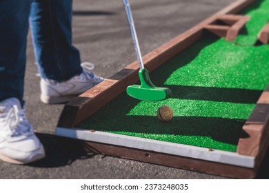 Mini golf course, process of playing miniature golf on a green artificial turf in a summer sunny day, eqipment for mini-golf, club and ball