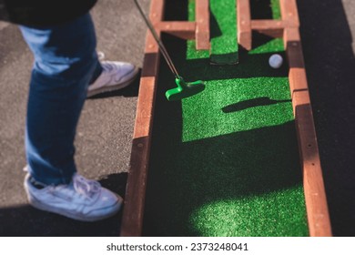Mini golf course, process of playing miniature golf on a green artificial turf in a summer sunny day, eqipment for mini-golf, club and ball