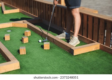 Mini golf course, process of playing miniature golf on a green artificial turf in a summer sunny day, eqipment for mini-golf, club and ball