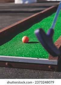 Mini golf course, process of playing miniature golf on a green artificial turf in a summer sunny day, eqipment for mini-golf, club and ball