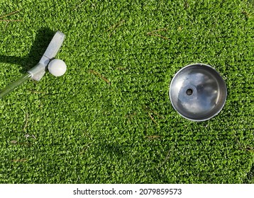 Mini Golf Putter And Ball Near The Hole On Artificial Grass Playing Track. Aiming On A Miniature Golf Course.