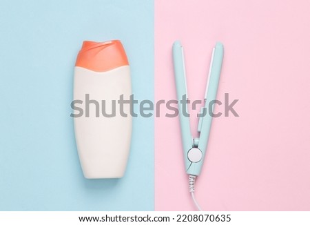 Mini hair straightener with a bottle of shampoo on a blue pink background. Hair style. Top view