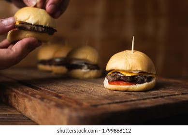 Mini homemade burger with cheddar cheese, tomato and mayonnaise to eat them as snacks. Hands grabbing a burger in the background. Horizontal image with space for text.