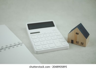 A Mini House Made Of Wood And A Calculator Placed Near A Notebook. The Concept Of Calculation Of Cost Buy Or Rent Home