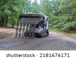 The mini loader Bobcat tractor moves and unloads gravel on the old road reconstruction site
