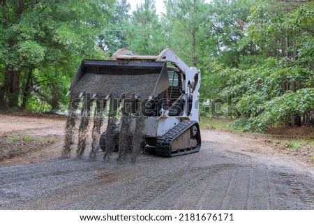 The mini loader Bobcat tractor moves and unloads gravel on the old road reconstruction site