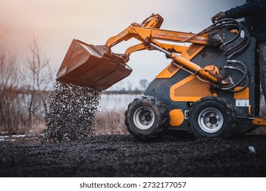 Mini loader with bucket. Mini loader is preparing the terrain. Mini wheel loader is spreading the stone onto the work surface.