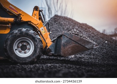 Mini loader with bucket. Mini loader is preparing the terrain. Mini wheel loader is spreading the stone onto the work surface.