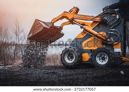 Mini loader with bucket. Mini loader is preparing the terrain. Mini wheel loader is spreading the stone onto the work surface.