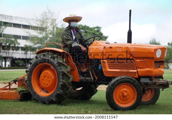 Mini orange-\
colored tractor that Asian man drives to mow lawn in front of the\
building. Concept : Vehicle for agriculture and various  using. \
Convenient and compact.          \

