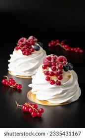 Mini Pavlova cake with raspberry, blueberry and red currant on black background
