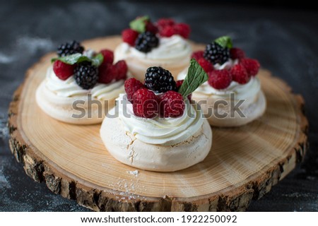 Mini Pavlova with raspberry and blueberry on a wooden plate with black background