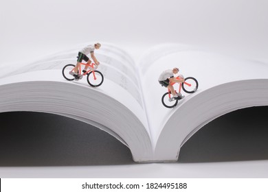 A Mini People,  Small Figures Cycling On Open Book