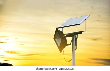 Mini Photovoltaic Or Solar Cell Panel And Floodlight Led Installed On Metal Pole Against Sunset Sky To Store And Save The Energy From The Sun To Use The Light At Night Around The House Or The Park.