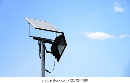 Mini Photovoltaic Or Solar Cell Panel And Floodlight Led Installed On Metal Pole Against Blue Sky To Store And Save The Energy From The Sun To Use The Light At Night Around The House Or The Park.