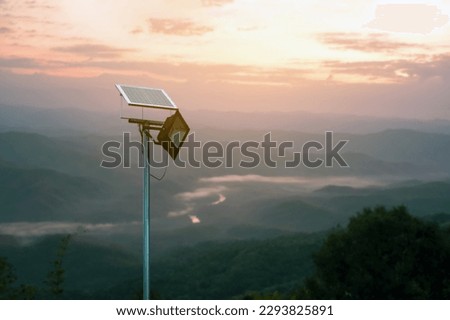 Mini photovoltaic or solar cell panel installed on metal pole with hd floodlight to store and use the power from the sunlight at night around house on the mountain, blurred sunset mountain background.