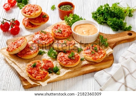 mini pizzas with ham and pecorino cheese on wooden cutting board with thousand islands sauce on white wooden table, picnic appetizer, horizontal view from above