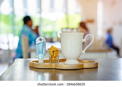 Mini Portable Alcohol Gel Bottle To Kill Corona Virus(Covid-19) And Biscuits And Coffee Cup On Table With Blurred Image Of A Family Eating At Restaurant In Background. Health Care Concept.