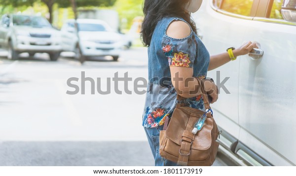 Mini\
portable alcohol gel bottle to kill Corona Virus(Covid-19) hang on\
a leather shoulder bag of a woman while open a car door to travel.\
New normal lifestyle.Selective focus on alcohol\
gel