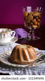 Mini Pound Cake - Almond Lemon Drizzle On Old Pictures Coffee Cup, Side Plate On Lace And Glass Full Of Almonds And Hazelnuts, Purple Background