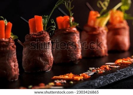 Mini roast beef rolls with vegetables, on a black slate plate, on a black background. Fusion food concept, low key, copy space