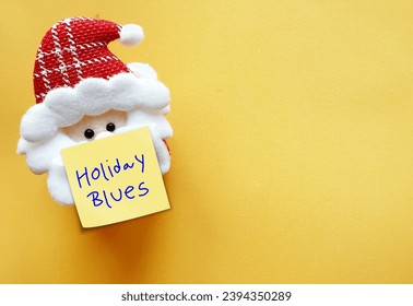 Mini santa on yellow copy space background with note written Holiday Blues -  feeling of sadness that occur during Christmas festive seaso - anxiety, depression, loneliness or negative emotions