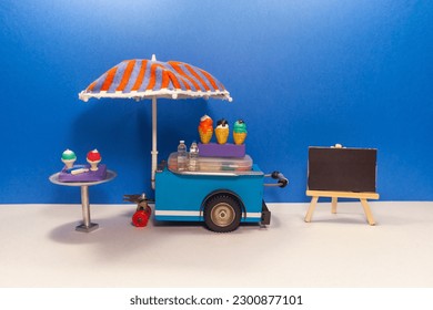 Mini shop Ice cream cart with blue red umbrella. Assortment of ice cream empty menu black chalkboard. blue wall background.