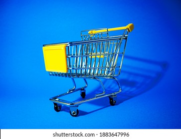 Mini shopping cart on blue background, empty yellow trolley
