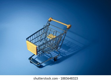 Mini shopping cart on blue background, empty yellow trolley top view