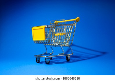 Mini shopping cart on blue background, empty yellow trolley, side view
