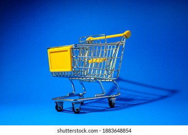 Mini shopping cart on blue background, empty yellow trolley, side view