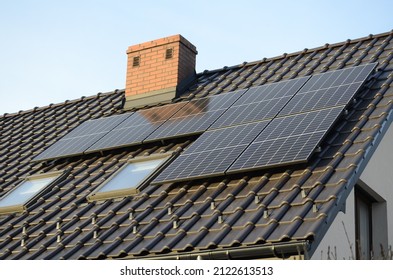 Mini small blue solar panels installation on a dark roof of a house during sunny day in a Poland city.