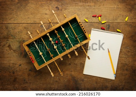 Mini soccer game and a blank note pad, on an old wooden table. Tactics, game planning concept. 