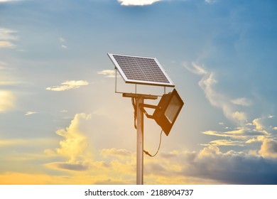 Mini solar cell or photovoltaic panel and floodlight led installed on metal pole, blurred clouds and sunset background, concept for storing and using the natural power with streetlight at night.