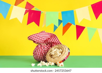 Mini sombrero with popcorn, bundle bag and flags for Festa Junina celebration on table against yellow background