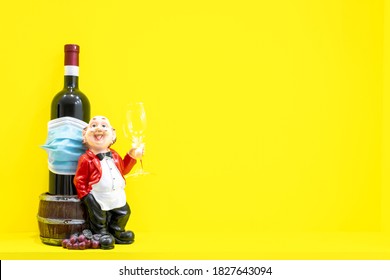 Mini Statue of servant holding empty glass with bottle coverer with medical face mask. Copy space image with yellow background. Concept of social events during pandemic and corona virus quarantine.