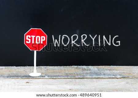 Mini STOP sign over chalkboard background and table, STOP WORRYING concept