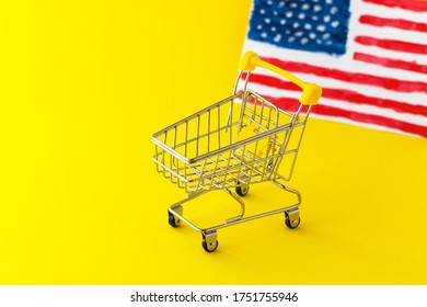 Mini Supermarket Shopping Cart And Abstract Hand Drawn American Flag On Yellow Background. Import And Export Concept. E-commerce. US Food Delivery Service. Holiday Sale And Online Shopping.