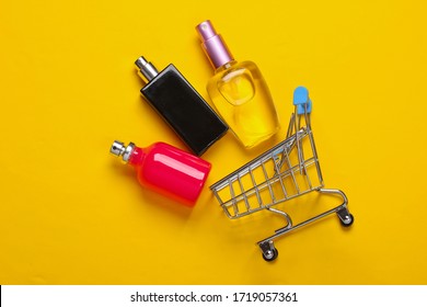 Mini supermarket trolley with perfume bottles on a yellow background. Top view, minimalism