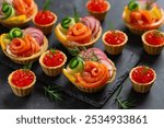 Mini tartlets with salmon red caviar and smoked salmon, cream cheese, cucumber and raddish, appetizers idea for holidays table, charcuterie, black background