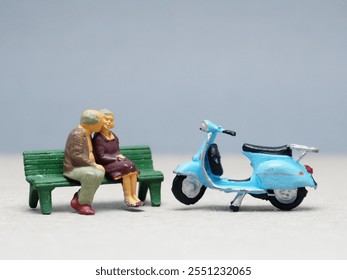 Mini toy of action figure at outdoor with blurred background. Toy photography concept design. Minifigure of old couple character sitting on the bench with blue vintage motor. Romantic scene at garden. - Powered by Shutterstock