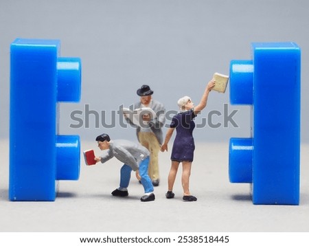 Mini toy of action figure at table with blurred background. Macro toy photography concept design. Minifigure of young people character at library to take a book from rack.