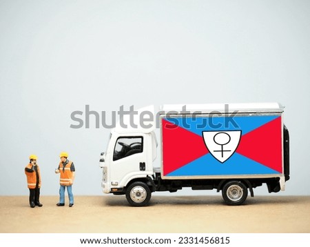 Mini toy at table with white background. Industrial shipping concept. Other World Kingdom flag design, commercial BDSM and femdom facility, resort, and purported micronation.