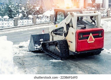 Mini tractor ski steer loader machine clean dirty snow of drive way. Cleaning city street, removing snow ice at heavy snowfalls and blizzard. Snowplow outdoors clean pavement sidewalk road driveway