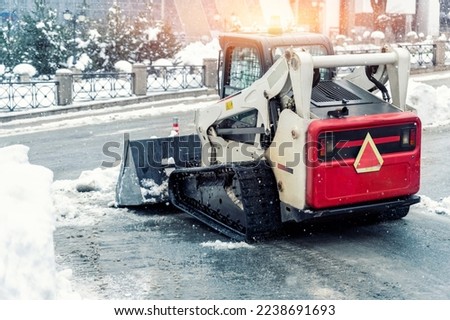 Mini tractor ski steer loader machine clean dirty snow of drive way. Cleaning city street, removing snow ice at heavy snowfalls and blizzard. Snowplow outdoors clean pavement sidewalk road driveway