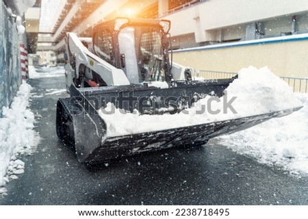 Mini tractor ski steer loader machine clean dirty snow of drive way. Cleaning city street, removing snow ice at heavy snowfalls and blizzard. Snowplow outdoors clean pavement sidewalk road driveway