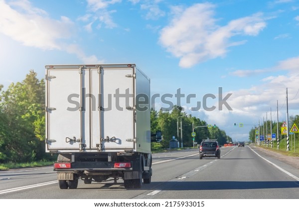 Mini truck driving on highway on sunny day. White\
modern delivery small shipment cargo courier truck moving fast on\
motorway road to city urban suburb. Busines distribution logistics\
express service