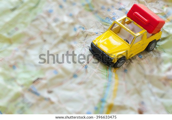 Mini yellow car with red suitcase on a jammed\
map. Closeup