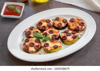 Mini Zucchini Pizza Bites. Grilled Zucchini Slices With Sausage And Melted Mozzarella Cheese Served On A White Plate With Tomato Sauce And Fresh Basil Leaves