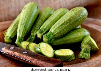 Mini zucchinis on a wooden board with a knife and a rustic fabric background